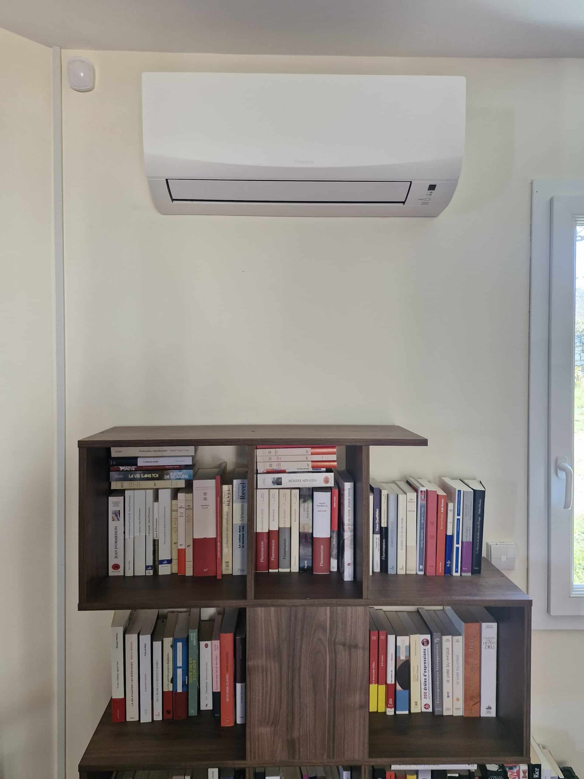 Climatiseur Daikin blanc au-dessus d'une bibliothèque en bois sombre remplie de livres sur un mur blanc.