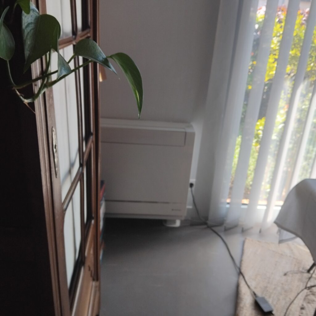 Coin salon lumineux avec plante verte et radiateur blanc Plante pothos sur buffet en bois, radiateur blanc et fenêtre lumineuse avec stores verticaux en arrière-plan.