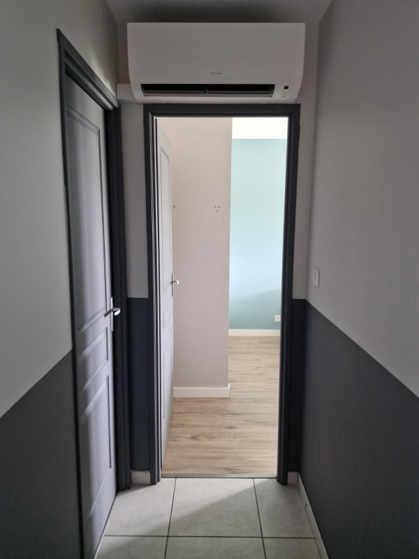 Couloir moderne avec climatiseur Daikin au-dessus d'une porte, murs bicolores et sol carrelé.