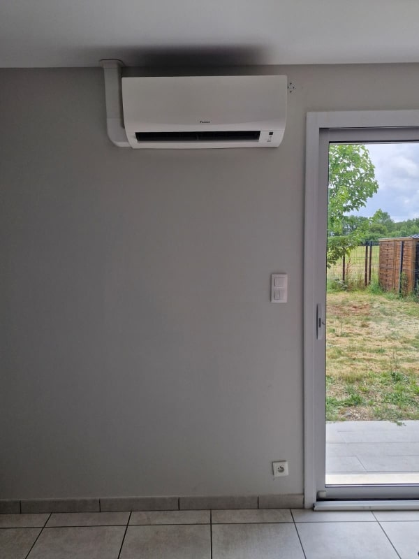 Climatiseur mural Daikin blanc installé sur un mur gris intérieur à côté d'une porte-fenêtre.