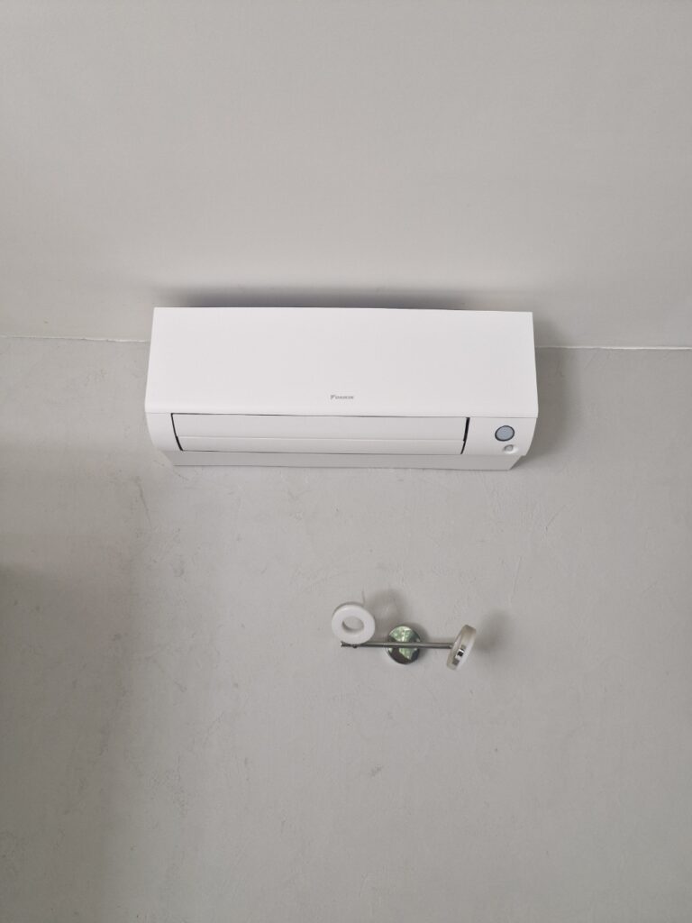 Climatiseur mural blanc Daikin installé sur un mur gris texturé au-dessus d'un luminaire design.