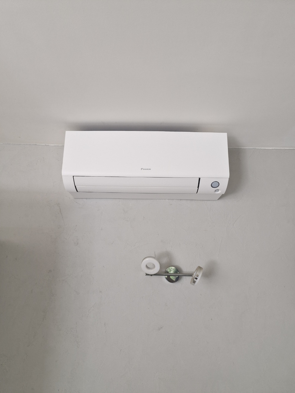 Climatiseur mural blanc Daikin installé sur un mur gris texturé au-dessus d'un luminaire design.
