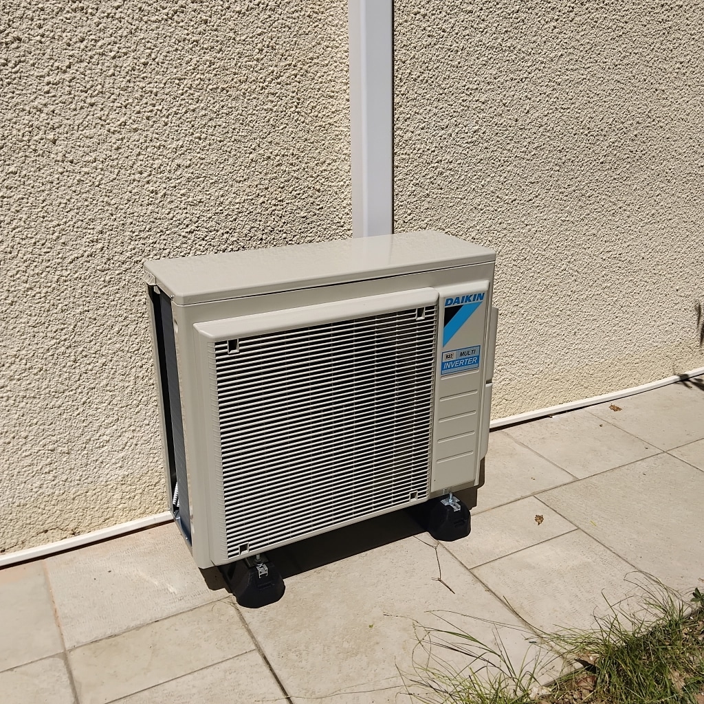 Unité extérieure Daikin Multi Inverter : installation fixe Unité extérieure Daikin Multi Inverter sur terrasse contre un mur beige.