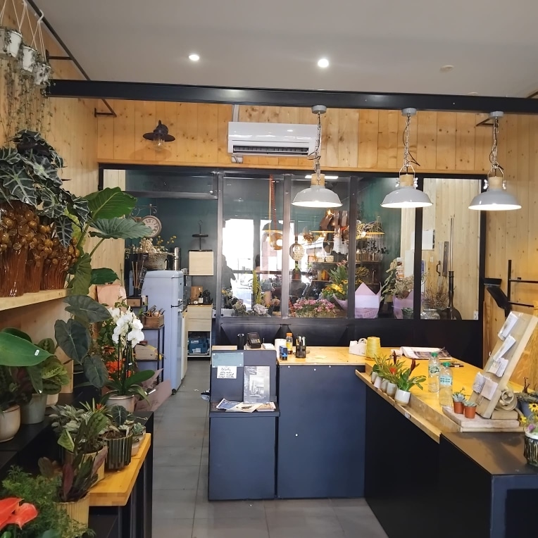 Boutique de Fleurs Design : Décoration Végétale et Bois Boutique de fleurs lumineuse avec plantes vertes, orchidées et comptoir en bois sous des luminaires industriels gris.