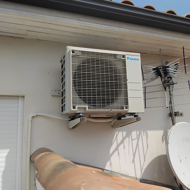 Unité de climatisation Daikin blanche fixée sur mur extérieur avec supports et conduits.