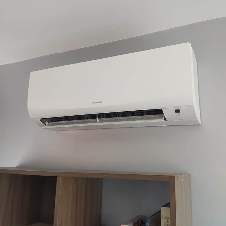 Climatiseur mural Daikin design blanc pour intérieur Climatiseur mural blanc Daikin fixé sur un mur gris au-dessus d'une bibliothèque en bois.