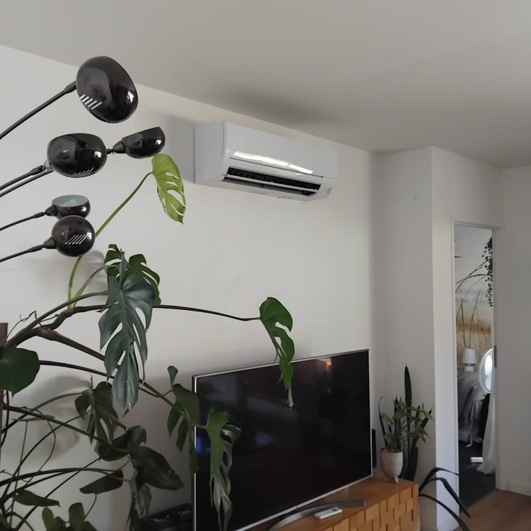 Climatiseur mural blanc : confort et design dans le salon Climatiseur mural blanc au-dessus d'une TV, grande plante monstera et lampadaire noir dans un salon moderne.